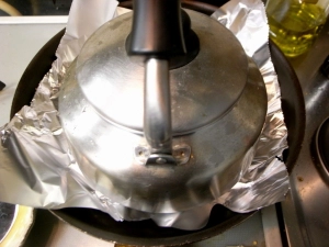 肉の上にアルミホイルをを広げ、水を入れたやかんをのせる