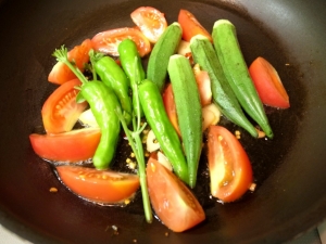 オリーブオイルにニンニク、唐辛子を加熱したらトマト、シシトウ、オクラ、バジルの茎を入れる