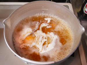 沸かせたつゆに卵を入れる