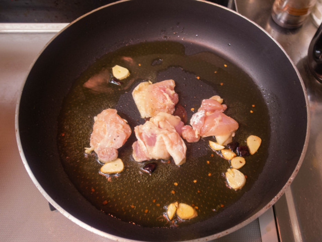 オリーブオイルでニンニクと唐辛子を熱し、香りが立ったら小麦粉をまぶした鶏肉を入れる