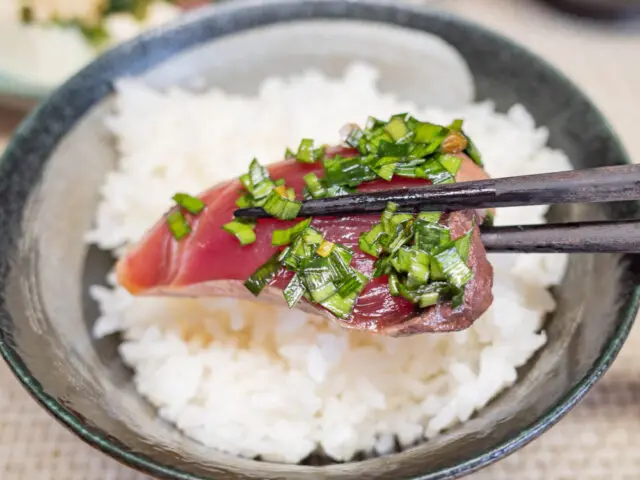 ニラ醤油をのせたかつおを白いご飯にのせようとしている写真