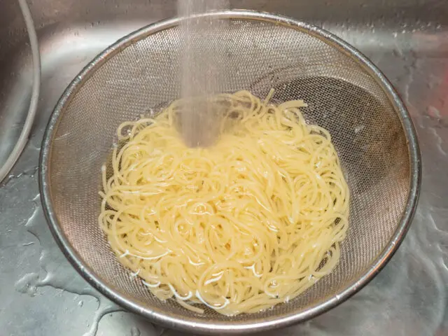 茹で上がったパスタを流水で冷やす写真