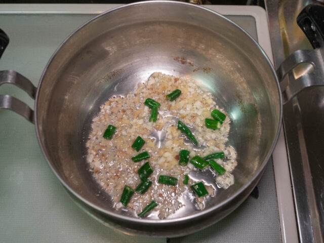 調理鍋にサラダ油を熱して、ニンニク、生姜、青唐辛子を炒める写真