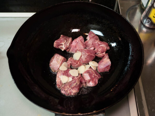 鍋にサラダ油を熱して、豚カシラとニンニクを炒める写真