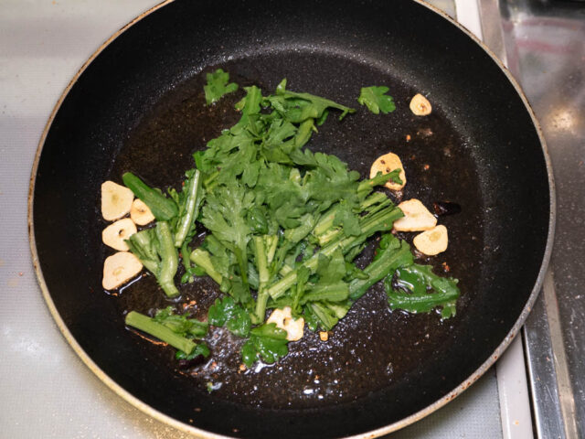 フライパンにオリーブオイル、ニンニク、唐辛子、春菊を入れて炒める写真