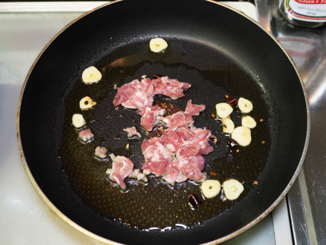 フライパンにオリーブオイル、ニンニク、唐辛子、豚肉を入れて炒める写真