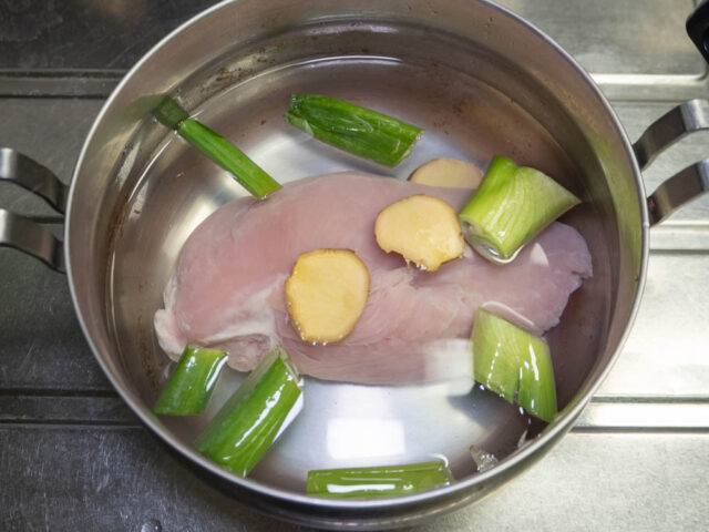 調理鍋に鶏胸肉、長ねぎ、生姜を入れて水を注いだ写真