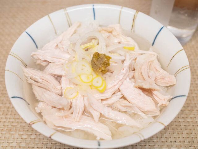 指で裂いた茹で鶏を温かい御飯にのせ、熱々に温めたスープを注ぎ、長ねぎと柚子胡椒を添えた写真