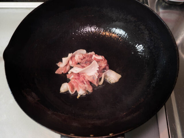 中華鍋にサラダ油を熱して豚肉を加えた写真