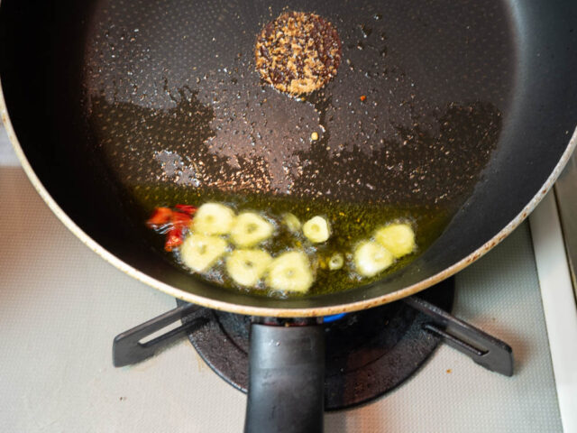 フライパンにオリーブオイル、ニンニク、唐辛子を入れて弱火で加熱する写真