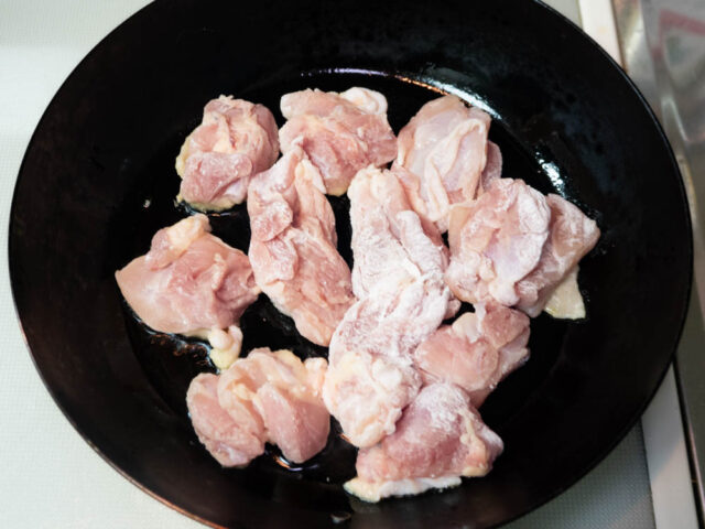サラダ油を熱したフライパンに片栗粉をまぶした鶏もも肉を入れた写真