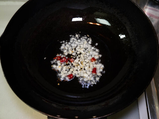 中華鍋にサラダ油を熱してニンニクと唐辛子を加えた写真