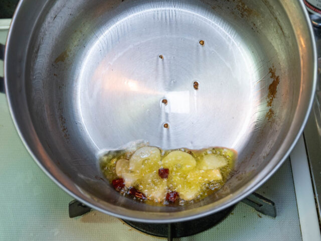 調理鍋にオリーブオイル、ニンニク、唐辛子を入れて弱火で加熱する写真