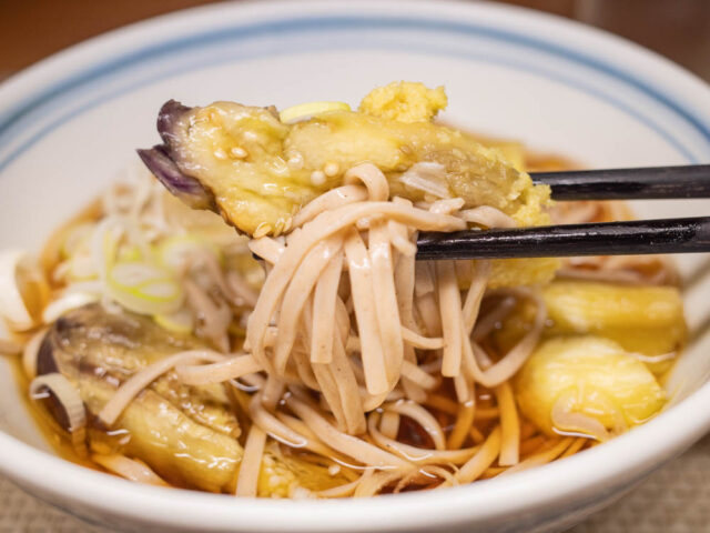 焼き茄子と蕎麦を箸で持ち上げた写真