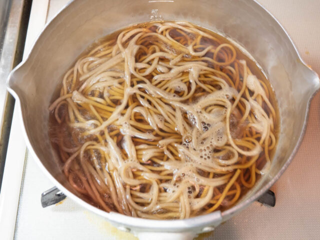 鍋につゆを沸かし、茹で蕎麦を温める写真