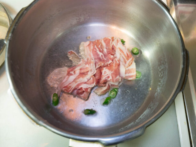 圧力鍋にサラダ油を熱して豚肉と青唐辛子を炒める写真