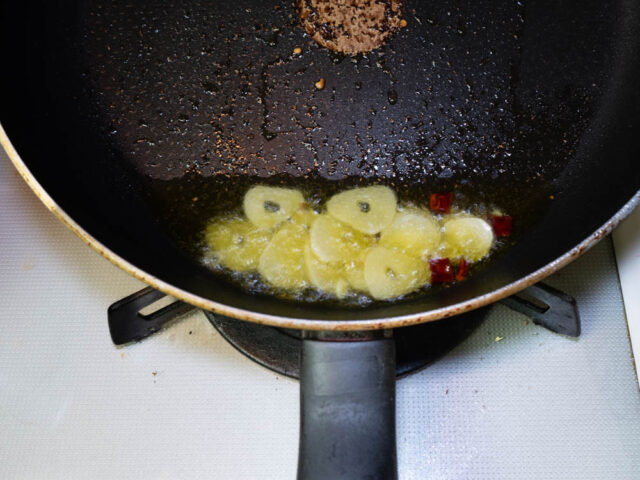 フライパンにオリーブオイル、ニンニク、唐辛子を入れて弱火で加熱する写真