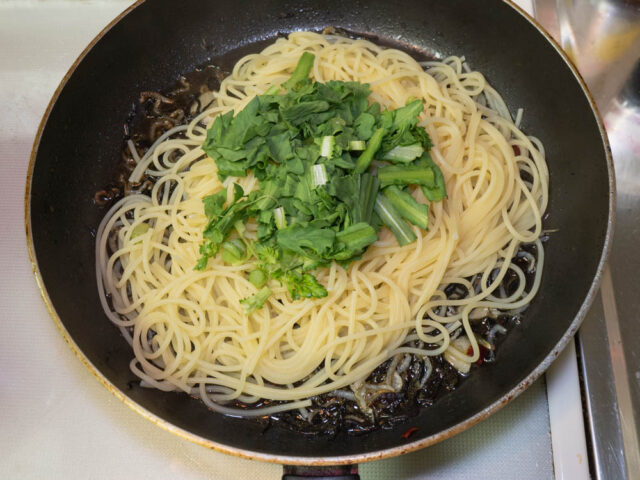 ソースのフライパンに茹で上がったパスタと春菊を加えた写真