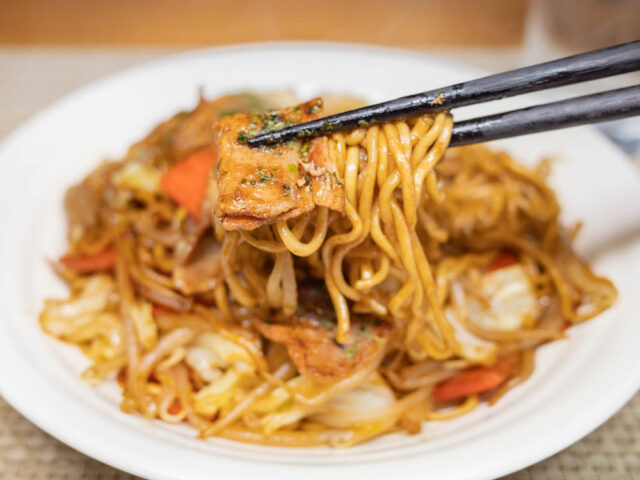 豚肉と焼きそば麺を箸で持ち上げた写真