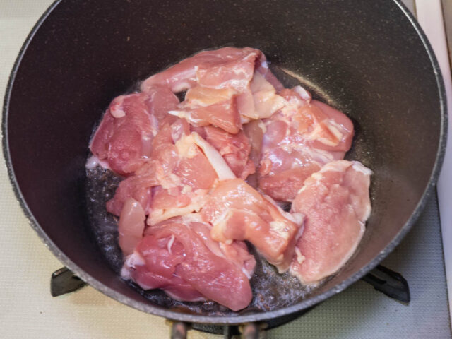 鍋にサラダ油を熱して、鶏もも肉を入れた写真