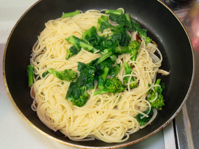 茹で上がったパスタと菜の花をソースのフライパンに合わせた写真