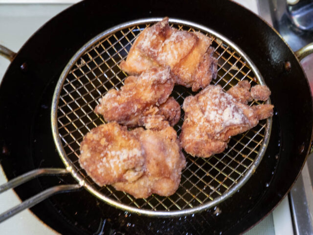 揚げざるで揚げた鶏肉を引き上げた写真