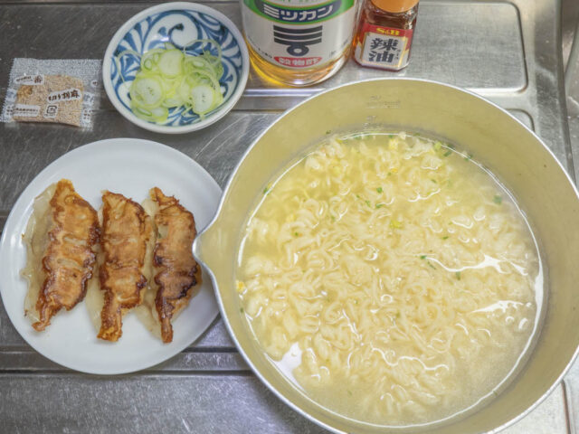 鍋につくったインスタントラーメンと餃子、長ねぎ、酢、ラー油の写真