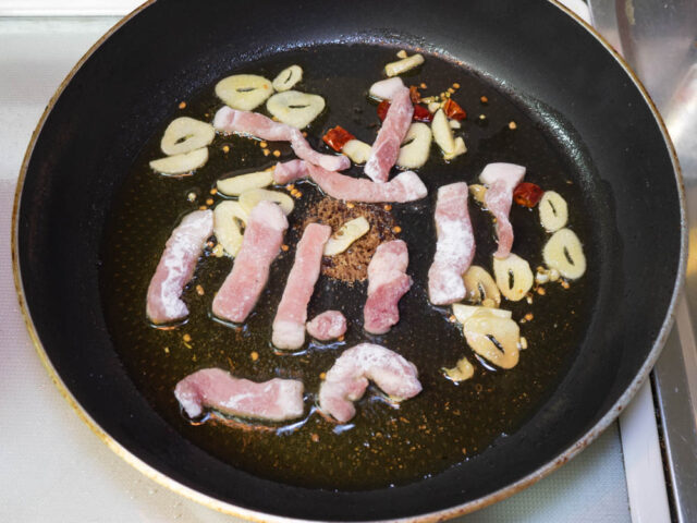 フライパンにオリーブオイル、ニンニク、唐辛子、豚肉を入れてて加熱する写真