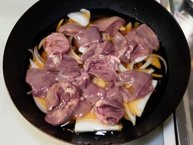 フライパンに水とめんつゆ、玉ねぎ、を入れ、その上に鶏もつを並べた写真
