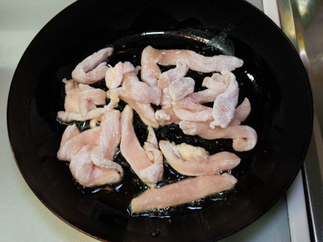 フライパンにごま油を熱して、片栗粉をまぶした鶏胸肉を炒める写真