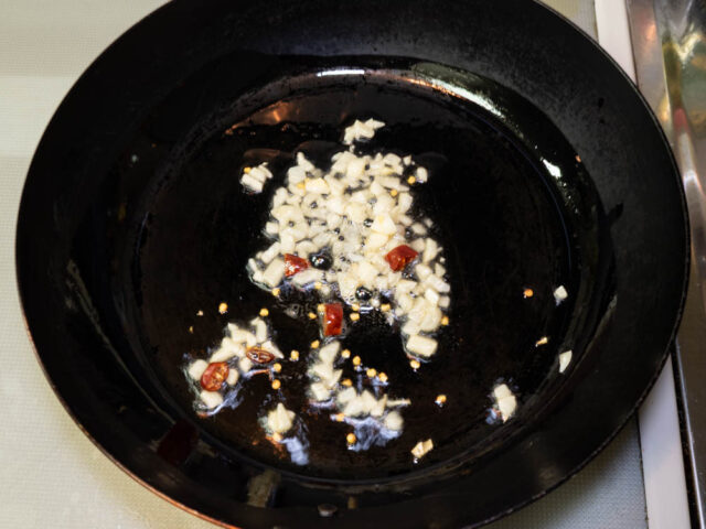 フライパンにごま油を熱して、ニンニクと唐辛子を入れた写真