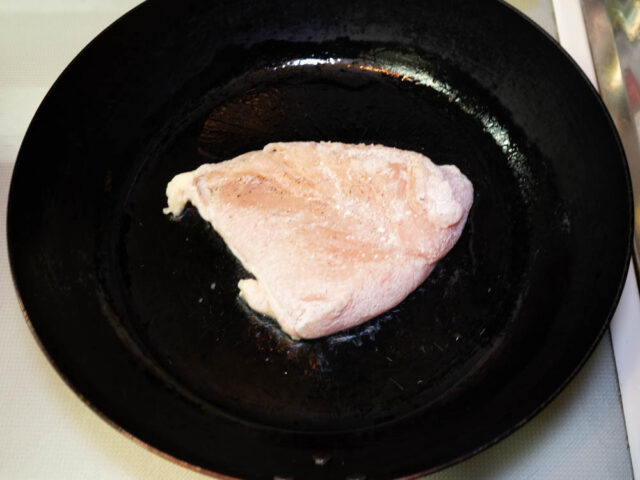 フライパンにサラダ油を熱して、小麦粉を叩いた鶏胸肉を入れた写真
