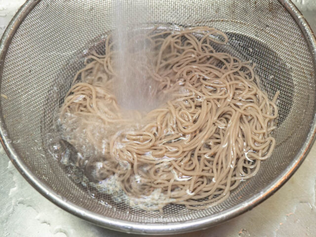 茹で上がった蕎麦を流水で洗う写真