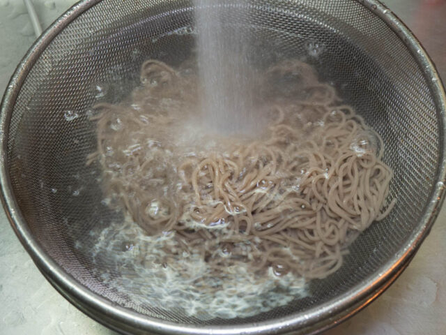 茹で上がった蕎麦を流水で洗う写真