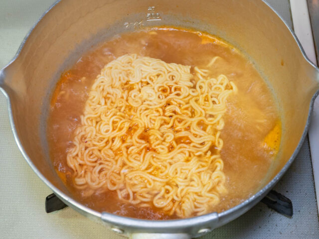 鍋にお湯を沸かし、粉末スープを溶かしてインスタント麺を入れた写真