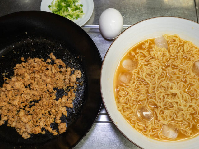 ラーメンを入れた丼、肉そぼろを炒めたフライパン、小口切りにした細ねぎ、生卵を並べた写真