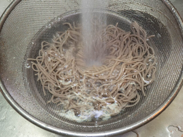 茹でた蕎麦を流水で洗う写真