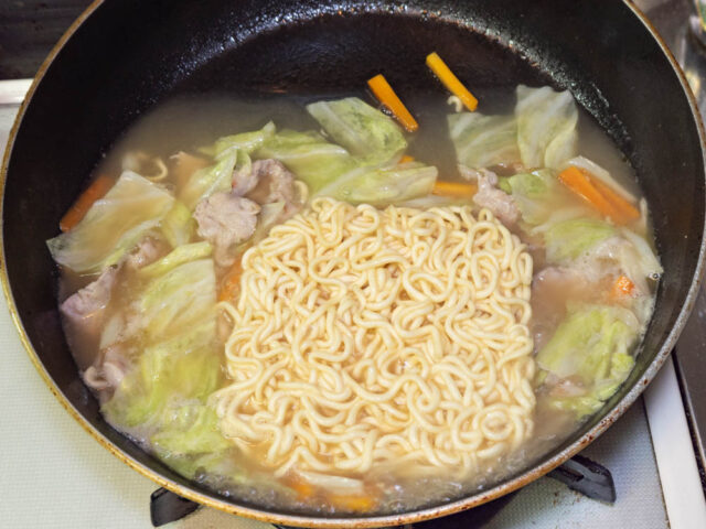 フライパンを傾けて麺を茹でる写真