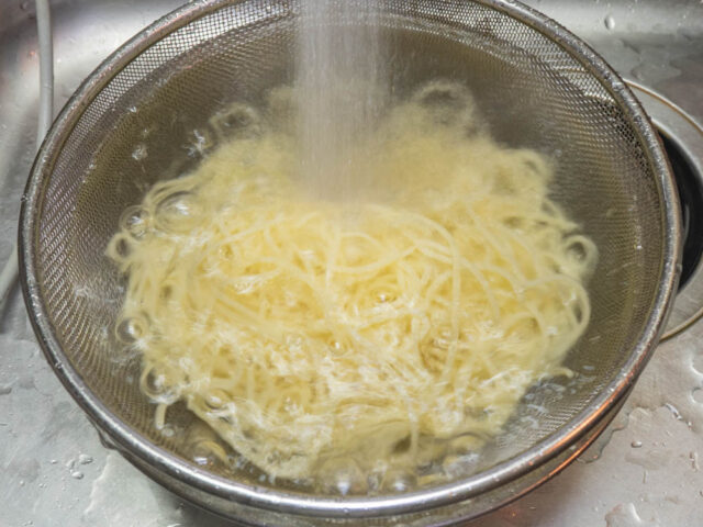 茹で上がったパスタを流水で冷やしている写真