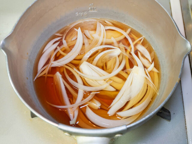 鍋に水、めんつゆ、玉ねぎを入れて火にかけた写真