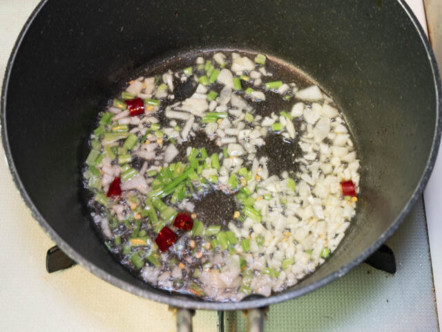 鍋にサラダ油を熱して、ニンニク、唐辛子、パクチーの茎を炒める写真