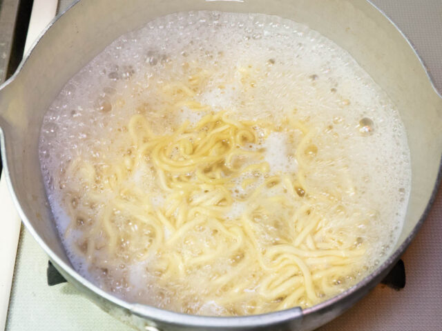 鍋にお湯を沸かしてインスタント麺を茹でる写真