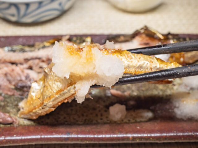 大根おろしをのせた秋刀魚の塩焼きを箸で持ち上げた写真
