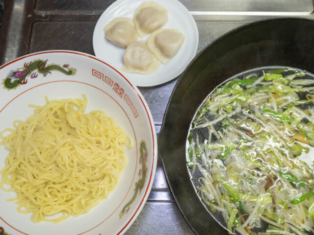 丼に入れた茹でた麺、水餃子、中華鍋のスープの写真
