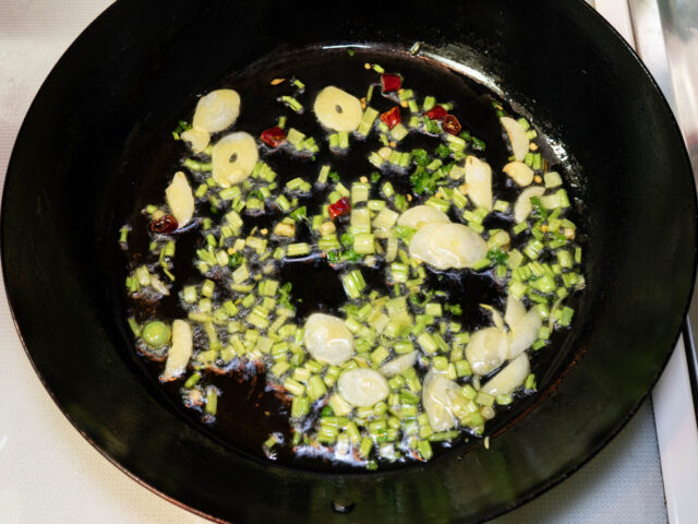 フライパンにオリーブオイル、パクチー、ニンニク、唐辛子を入れて弱火で加熱する写真