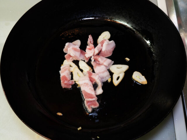 フライパンにサラダ油を熱し、ニンニクと豚肉を入れた写真