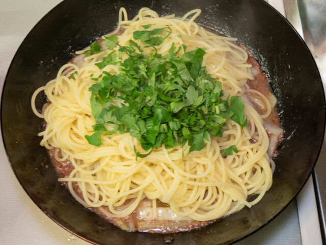 ソースのフライパンに茹で上がったパスタと刻んだパセリを加えた写真。