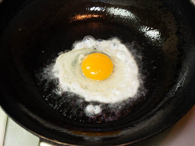 中華鍋にサラダ油を熱して、卵を割り入れた写真