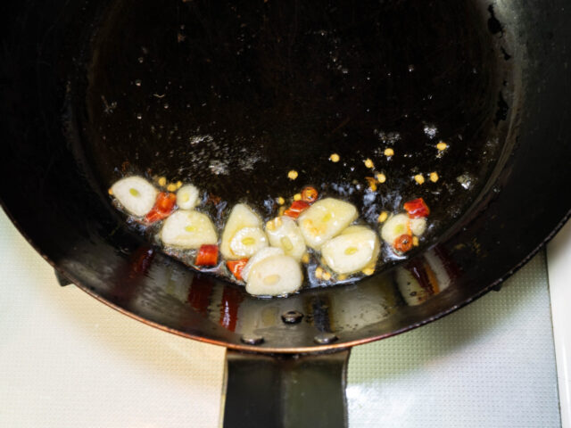 フライパンにオリーブオイル、オイルサーディンのオイル、ニンニク、唐辛子を入れて弱火で加熱する写真