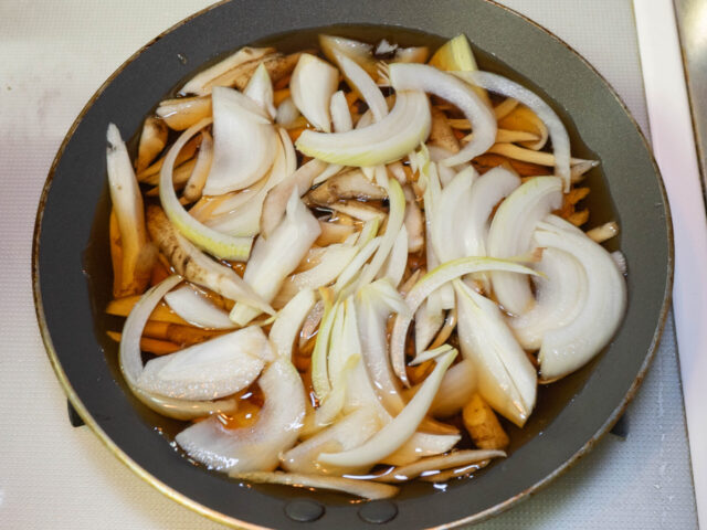 フライパンに水、めんつゆ、ごぼう、玉ねぎを入れて火をつけた写真